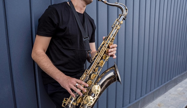 Joven músico callejero tocando el saxofón cerca de la gran pared azul