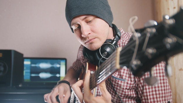 El joven músico compone y graba la banda sonora tocando la guitarra, usando computadora, auriculares y teclado, enfocándose en el equipo