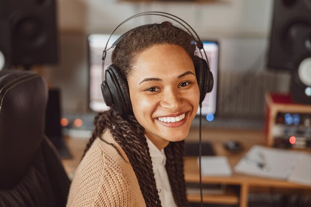 Joven músico compositor africano con auriculares en estudio de grabación sonriendo hermosa sonrisa con dientes mientras mira la cámara