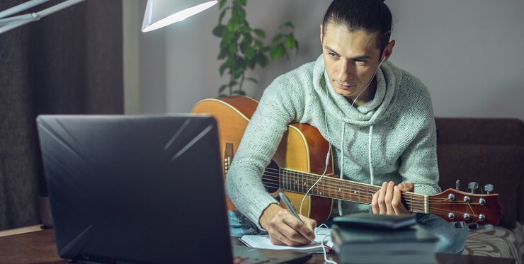 Foto joven músico está aprendiendo a tocar la guitarra acústica en una lección en línea usando una computadora portátil
