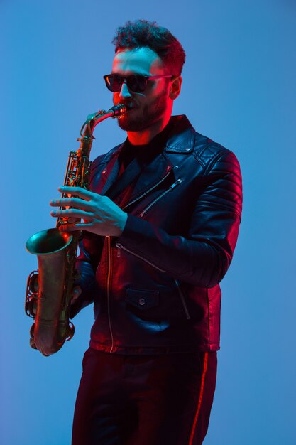 Foto joven músico de jazz caucásico tocando el saxofón en luz de neón