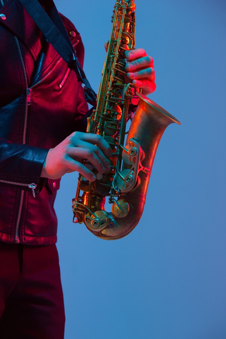 Foto joven músico de jazz caucásico tocando el saxofón sobre fondo de estudio azul-púrpura degradado en luz de neón. concepto de música, afición, festival. chico atractivo alegre. retrato colorido del artista.