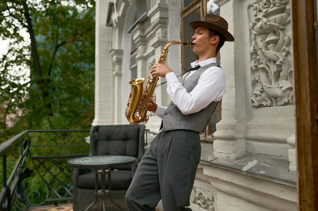 Joven músico masculino practicando saxofón en el balcón de su casa. Saxofonista inspirado tocando música