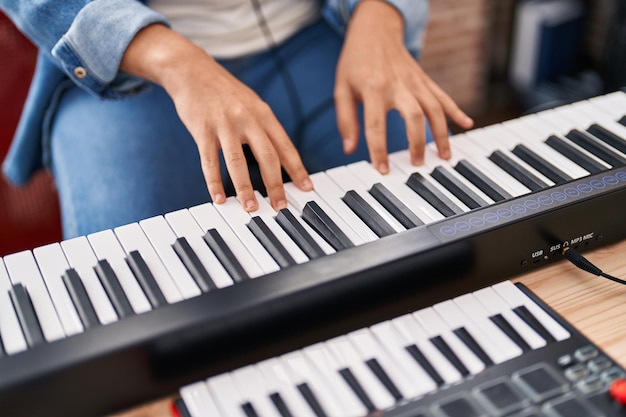 Joven músico no binario tocando el teclado del piano en el estudio de música