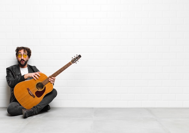 Joven músico sintiéndose sorprendido, feliz, asombrado y sorprendido, mirando a un lado con la boca abierta con un concepto de guitarra, rock and roll