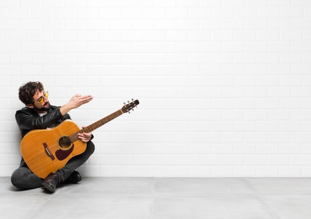 Joven músico sonriendo, saludándolo y ofreciéndole un apretón de manos para cerrar un trato exitoso, concepto de cooperación con una guitarra, concepto de rock and roll