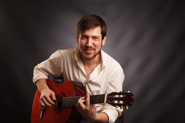 El joven músico toca la guitarra acústica y canta en un fondo oscuro