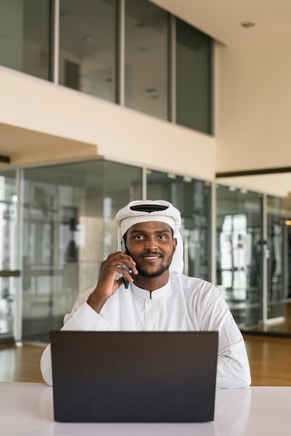 Joven musulmán africano usando computadora portátil y teléfono en la oficina