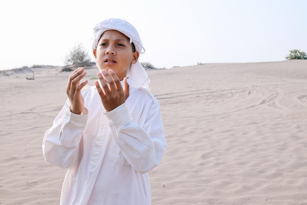 Joven musulmán asiático orando en las dunas de arena