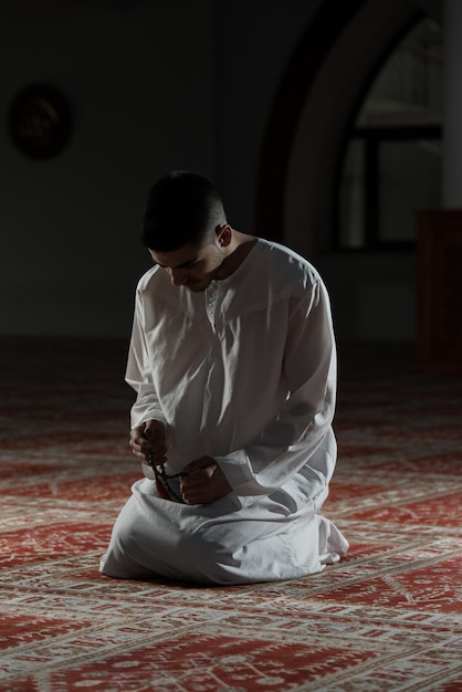 Joven musulmán haciendo oración tradicional a Dios mientras usa una gorra tradicional Dishdasha