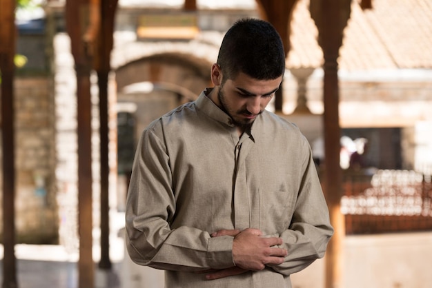 Joven musulmán haciendo oración tradicional a Dios mientras usa una gorra tradicional Dishdasha