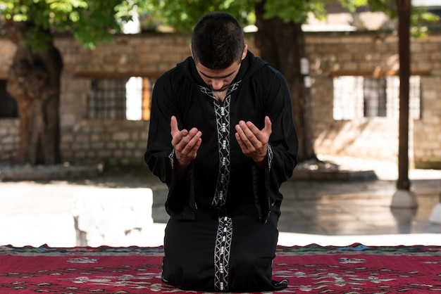 Joven musulmán haciendo oración tradicional a Dios mientras usa una gorra tradicional Dishdasha