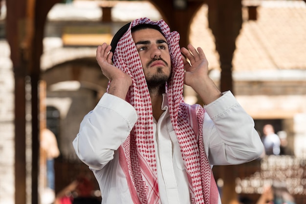 Joven musulmán haciendo oración tradicional a Dios mientras usa una gorra tradicional Dishdasha