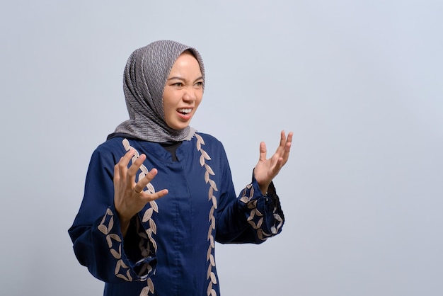 Una joven musulmana asiática enojada levantando las manos y gritando con rabia aislada sobre el fondo blanco