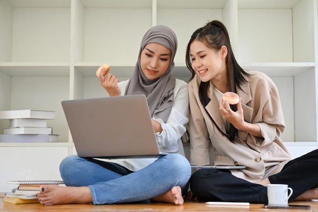 Una joven musulmana asiática en un espacio de coworking con su amiga comiendo donuts disfruta hablando