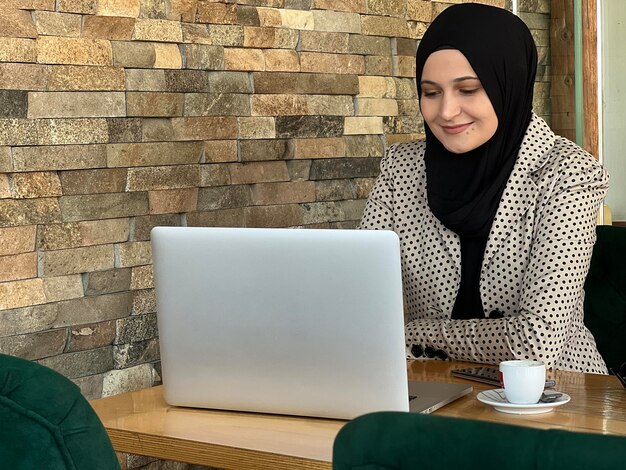 Una joven musulmana feliz con hiyab trabajando en una laptop en un café restaurante