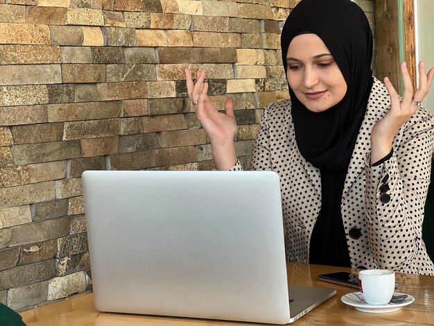 Una joven musulmana feliz con hiyab trabajando en una laptop en un café restaurante