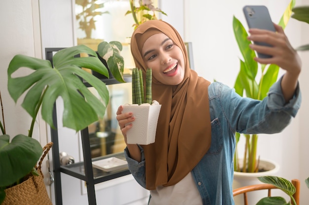 Una joven musulmana feliz tomando selfie con sus plantas y haciendo videollamadas en casa