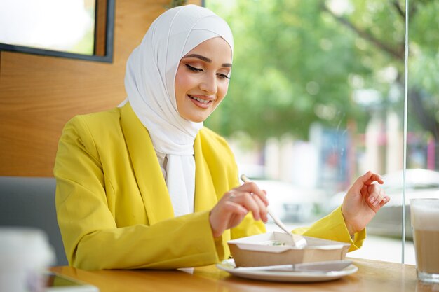 Joven musulmana en hijab almorzando en el café