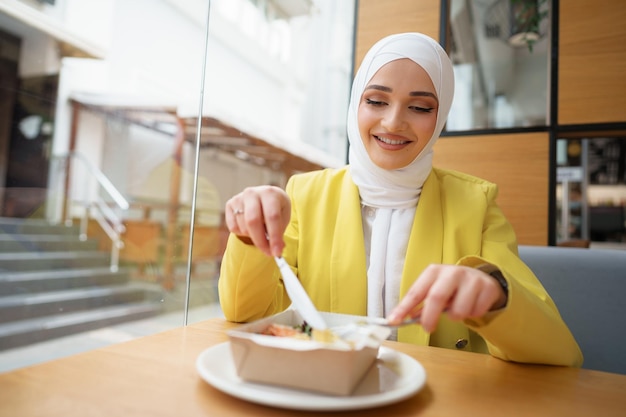 Joven musulmana en hijab almorzando en el café