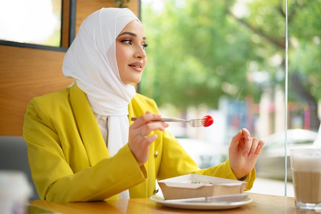 Joven musulmana en hijab almorzando en el café