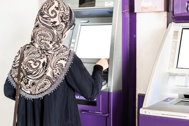 Foto joven musulmana con hijab retirar dinero del cajero automático.