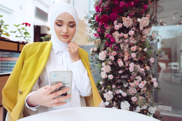 Joven musulmana en hijab con su teléfono inteligente en el café