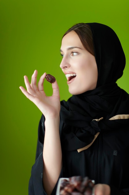 Joven musulmana con ropa musulmana tradicional sosteniendo dátiles secos. Niña árabe que representa el tiempo de iftar, el mes sagrado del ayuno, Ramadán Kareem