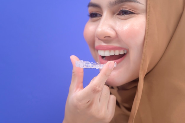 Una joven musulmana sosteniendo aparatos invisalign en estudio, salud dental y concepto de ortodoncia.