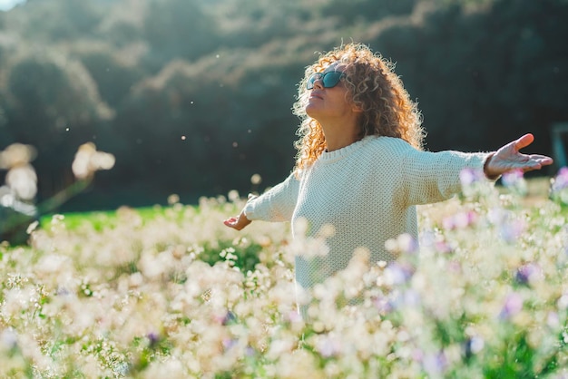 Joven muy contenta y emocionada abriendo los brazos extendidos en un prado de flores blancas Actividad de ocio al aire libre de verano Una mujer disfruta del parque natural Felicidad y estilo de vida saludable