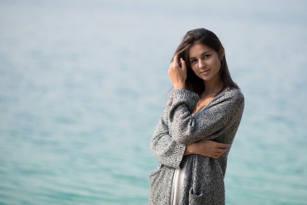 Joven muy hermosa con el pelo largo está de pie junto al lago. La niña admira el amanecer y disfruta del descanso.