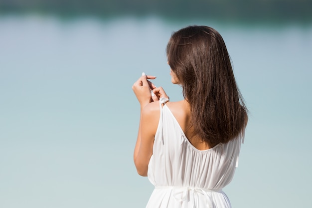 Joven muy hermosa con el pelo largo con un vestido blanco junto al lago. La niña está disfrutando el resto.