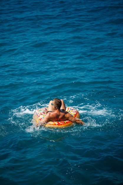 Un joven nada en mar abierto en un anillo inflable en un día soleado. Vacaciones de verano, turista de vacaciones.