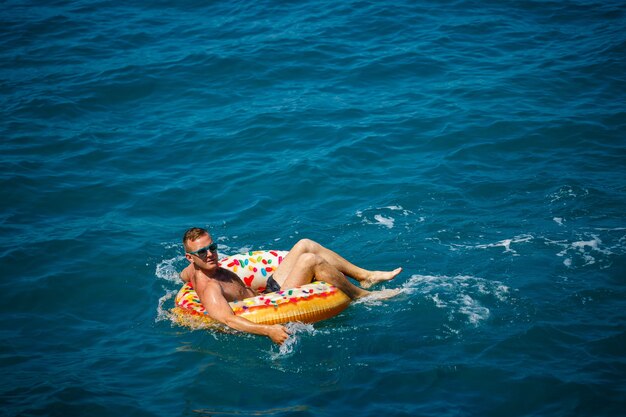 Un joven nada en mar abierto en un anillo inflable en un día soleado. Vacaciones de verano, turista de vacaciones.