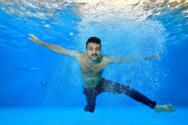 Un joven nada y posa bajo el agua en una piscina con un fondo azul