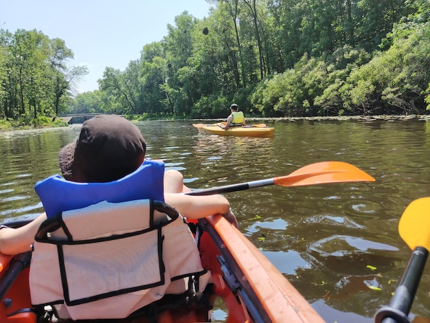 Foto un joven está nadando en un kayak con una paleta en un chaleco salvavidas en un río ancho deportes activos