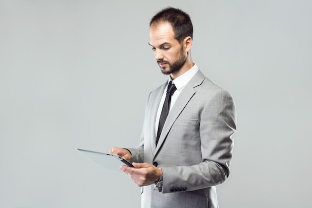 Joven de negocios utilizando su tableta digital sobre fondo gris.
