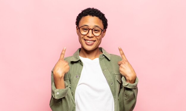 Joven negra afro con una mala actitud que parece orgullosa y agresiva, apuntando hacia arriba o haciendo un signo divertido con las manos