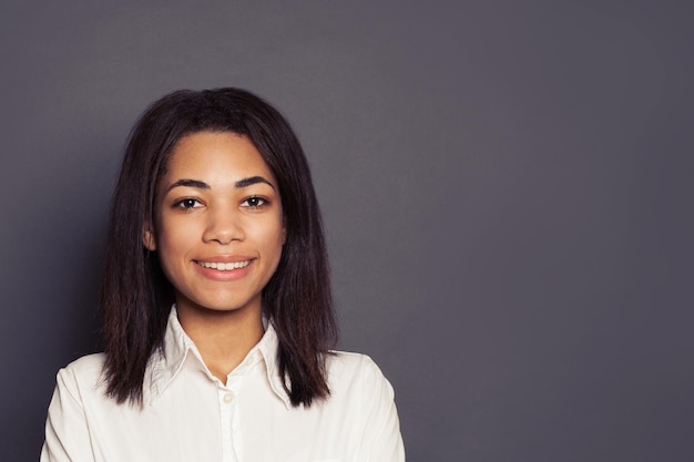 Una joven negra alegre sonriendo en un fondo gris cara de cerca