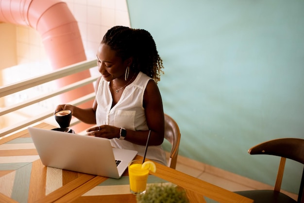 Joven negra bebiendo café mientras trabaja en una laptop en el café