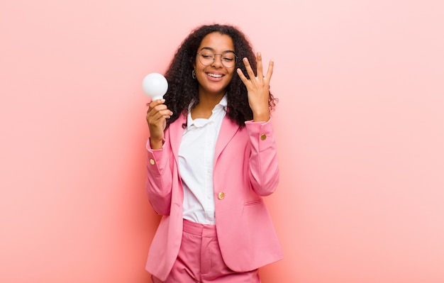 Joven negra con una bombilla de luz que tiene una idea en la pared rosa