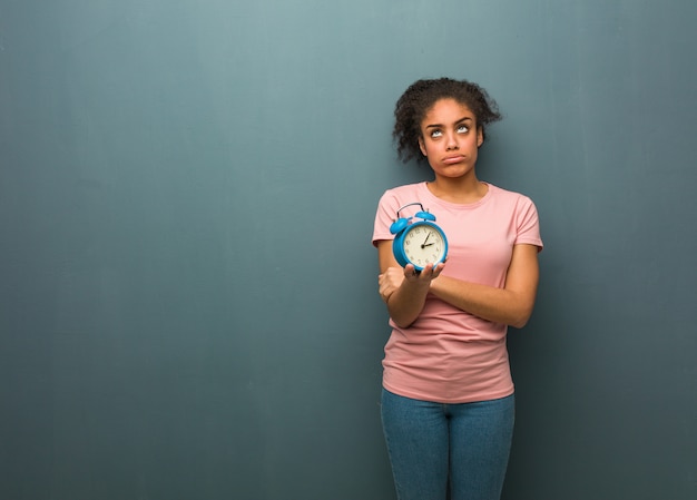 Joven negra cansada y aburrida. Ella está sosteniendo un reloj despertador.