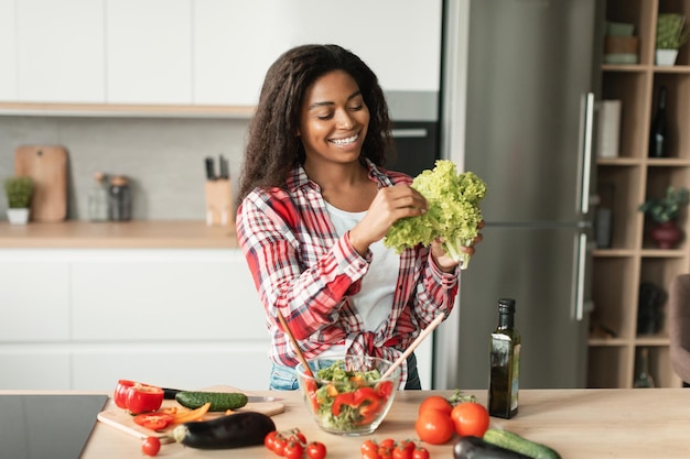 La joven negra feliz en una ensalada informal prepara comida a partir de verduras orgánicas se divierte