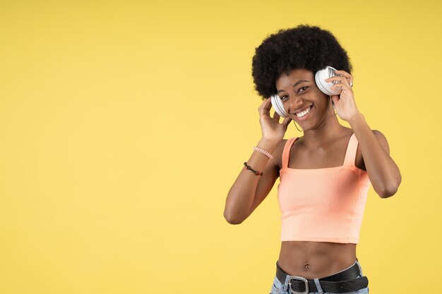 Joven negra feliz mientras sostiene sus auriculares blancos y escucha música