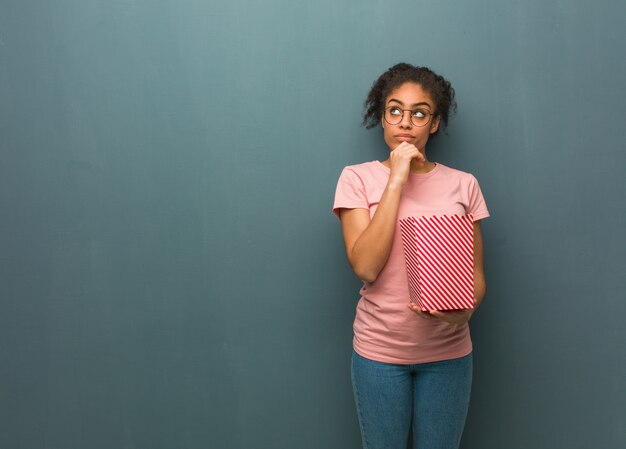 Joven negra pensando en una idea. Ella está sosteniendo un cubo de palomitas de maíz.