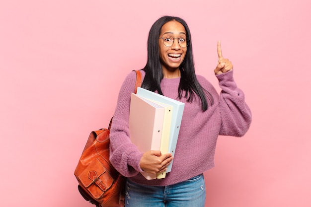 Joven negra que se siente como un genio feliz y emocionado después de darse cuenta de una idea, levantando alegremente el dedo, ¡eureka !. concepto de estudiante