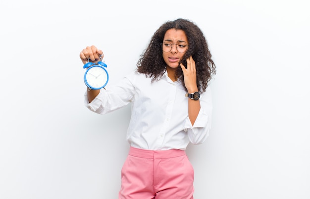 Joven negra con un reloj de alarma en la pared blanca