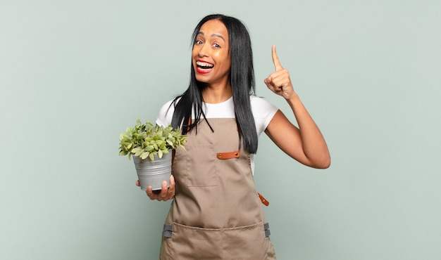 Joven negra sintiéndose como un genio feliz y emocionado después de realizar una idea, levantando alegremente el dedo, ¡eureka !. concepto de jardinero