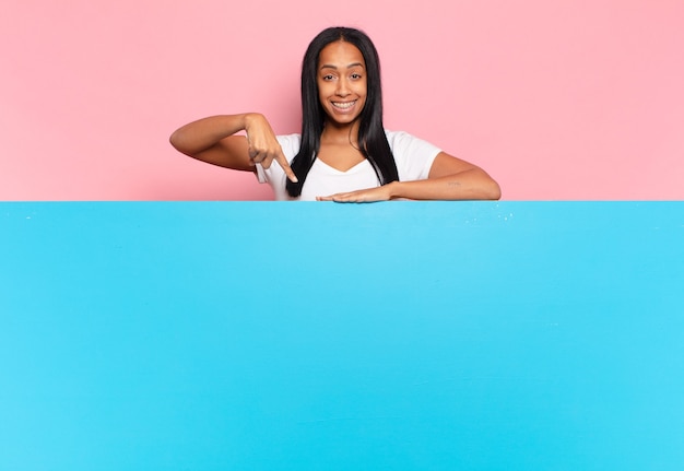 Joven negra sonriendo alegremente, sintiéndose feliz y apuntando hacia un lado y hacia arriba, mostrando el objeto en el espacio de la copia. concepto de espacio de copia