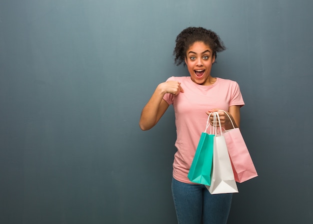 Joven negra sorprendida, se siente exitosa y próspera. Ella sostiene bolsas de la compra.